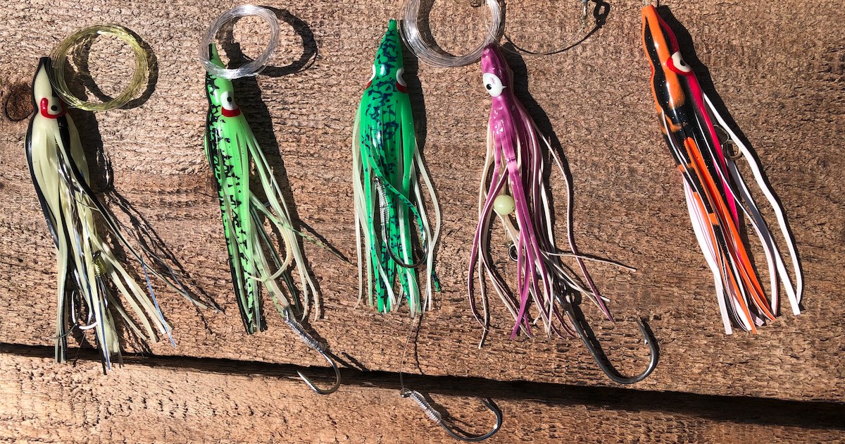 Five colorful salmon lures with various designs, including green, purple, and orange, displayed on a wooden surface.