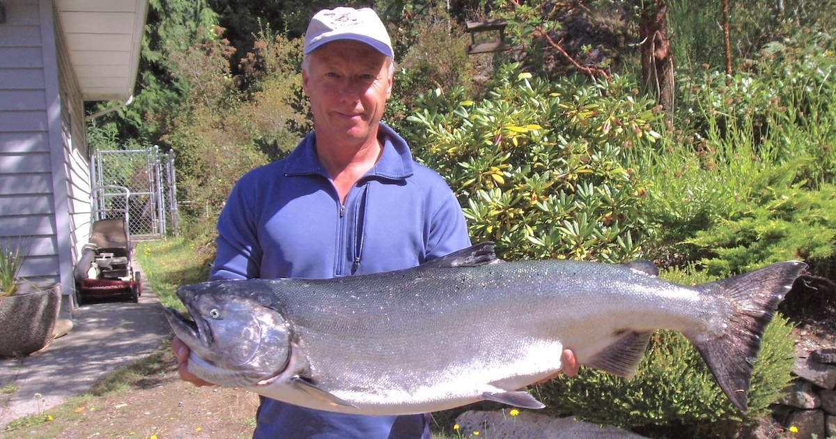 Man holding a large salmon fish outdoors, showcasing its size and features in a natural setting.