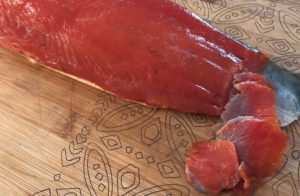 Sliced lox on a wooden cutting board, with a portion cut away from the main piece, showcasing its smooth texture and rich color.