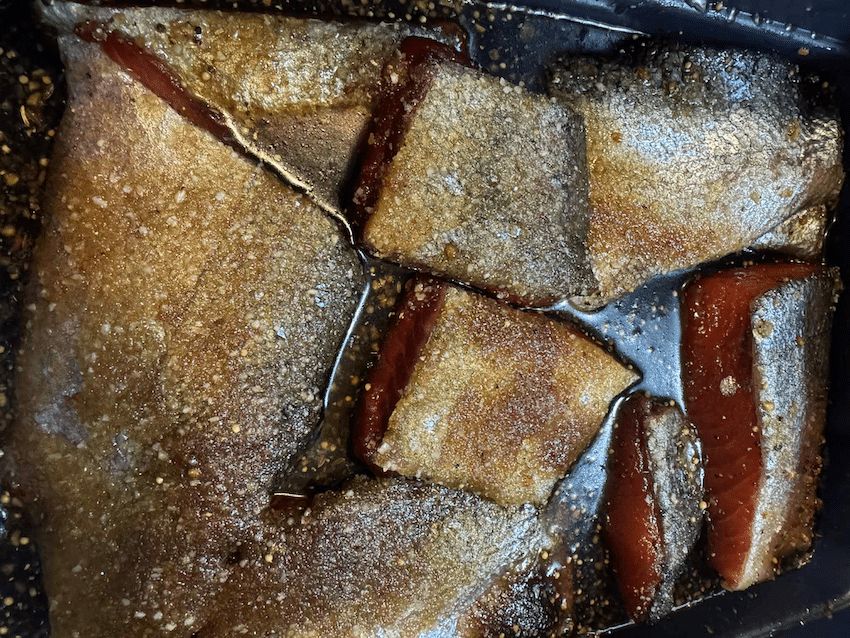 Close-up of salmon fillets being dry-cured with Demerara brown sugar and Montreal steak spice, showing moisture extraction.