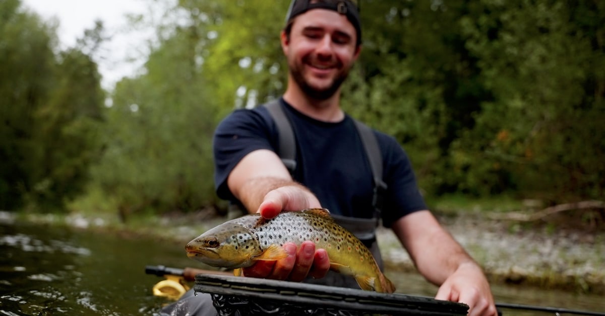 Angler Will Gillis holding a trout over a net, illustrating a fly fishing gear guide for matching rod weight to fish species.