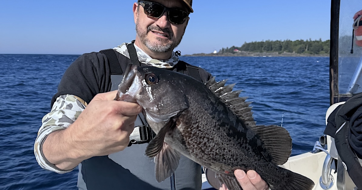 Angler holding a large black rockfish british columbia specimen on a fishing boat.