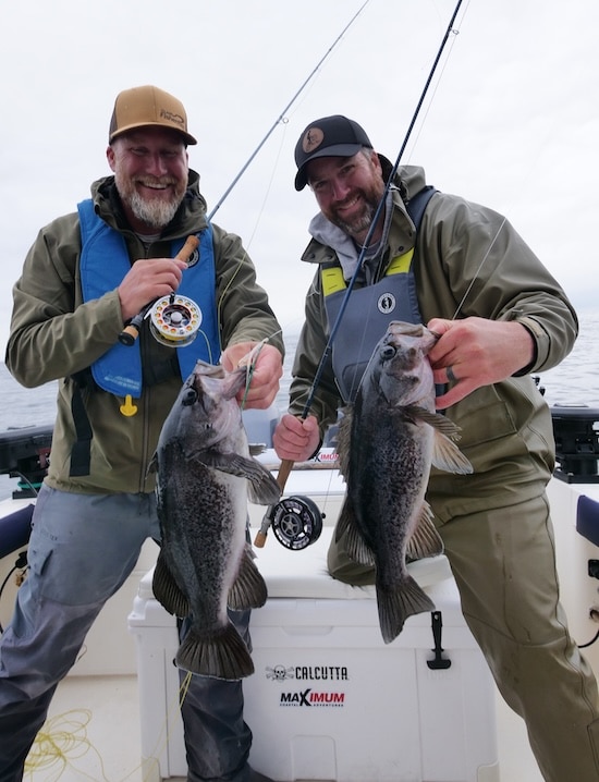 Two anglers holding black rockfish caught on fly rods in British Columbia waters.