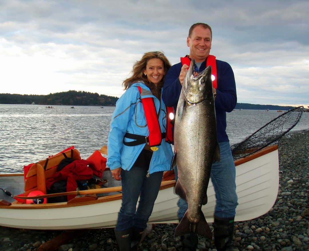 Darcy and Kate smiling on the Campbell River gravel beach beside their wooden rowboat showing how to catch a Tyee salmon