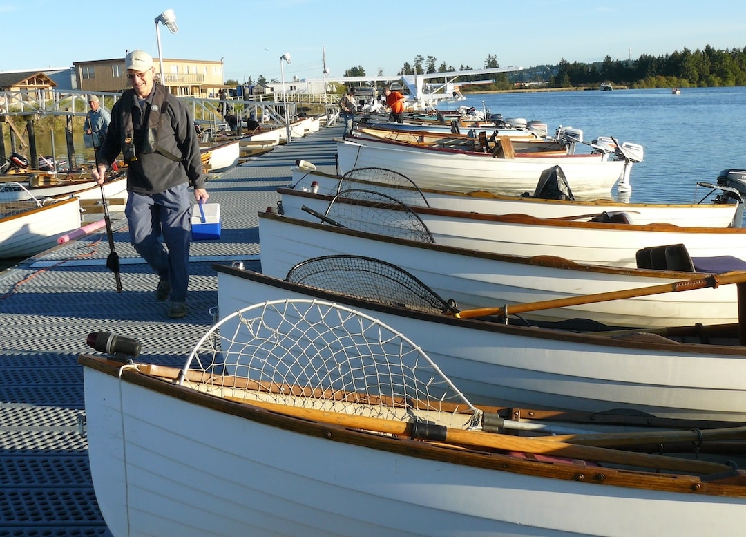 Angler walking down the Tyee Club dock lined with classic wooden rowboats and oars in Campbell River